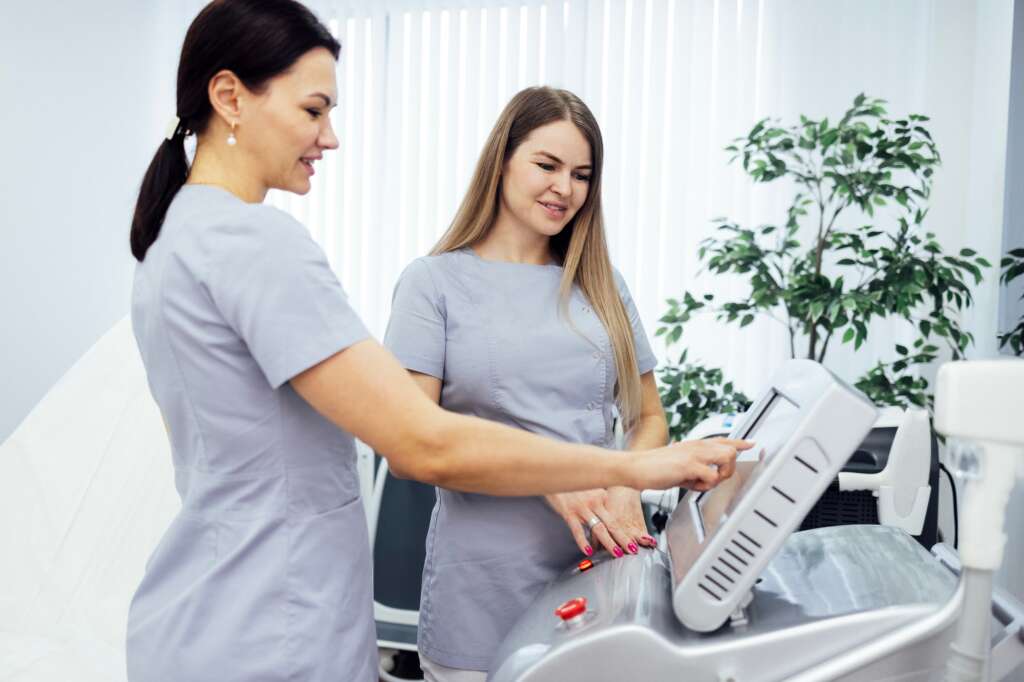 Woman cosmetologist touches screen of cosmetology equipment to set necessary parameters