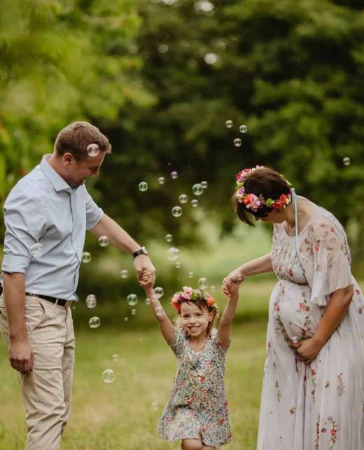 a man and woman standing in a grass field with a girl and bubbles